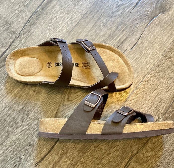 A pair of cork-sole sandals with adjustable straps, captured by a reviewer on a wooden floor