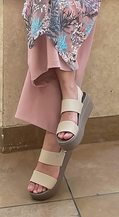 A reviewer wearing beige platform sandals paired with a floral dress, focusing on footwear for a shopping day look.