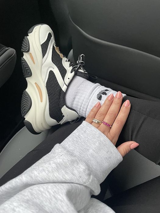 A reviewer sporting chunky Steve Madden sneakers in black, white, and nude tones.