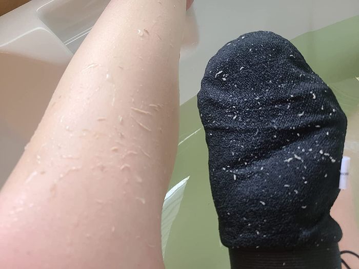 A reviewer exfoliating dry skin from their legs using a mitt