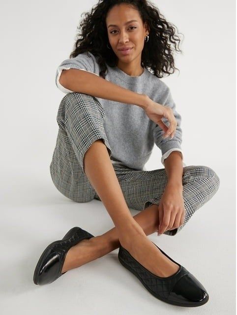 A person dressed in plaid pants and a grey top, wearing black quilted flats.