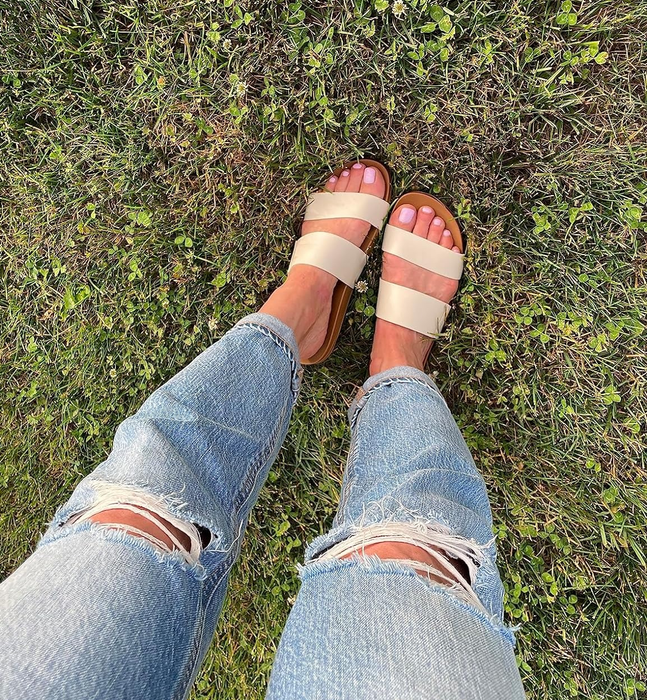 A reviewer rocking ripped jeans and beige strap sandals while standing on grass.
