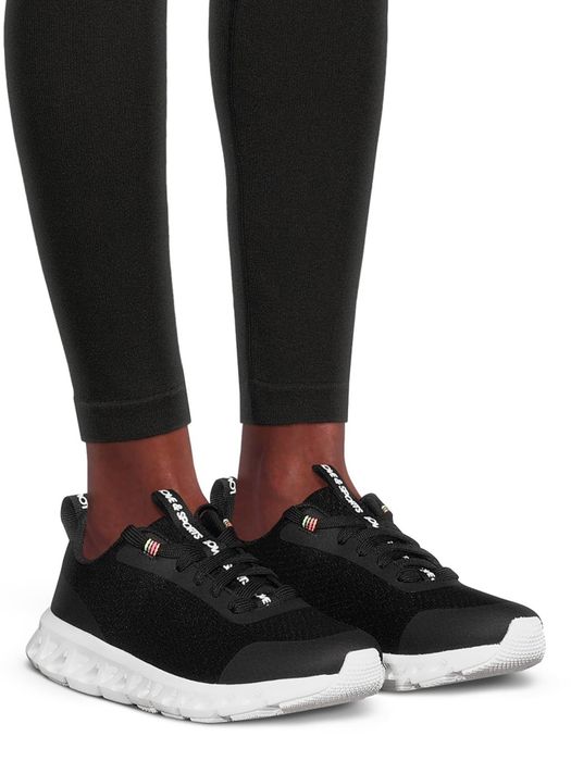 Close-up of a person wearing black sneakers with white soles, paired with black leggings