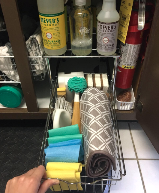 The reviewer pulls out a drawer, revealing three sponges, four magic erasers, two handheld scrub brushes, one dish brush, four folded dishcloths, and a folded drying pad, all neatly arranged.