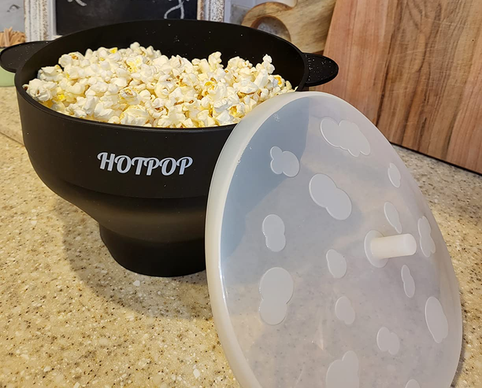 A bowl of popcorn resting on the countertop with the lid casually placed beside it.