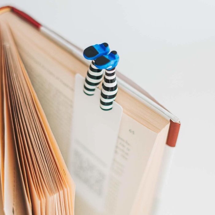 A bookmark with striped stockings and blue shoes at the ends of two legs, placed inside a book.
