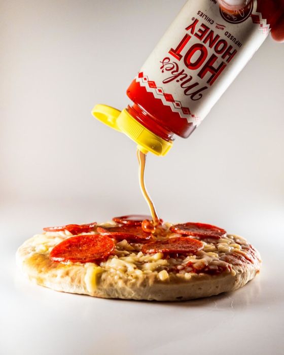 A reviewer drizzling honey over a pizza.