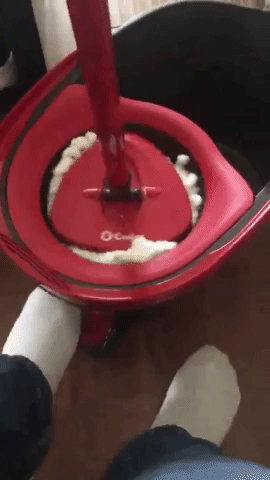 The reviewer is using a foot-operated pedal to wring out the microfiber mop.