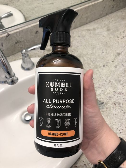 A person is seen holding an all-purpose cleaner in a bathroom setting.