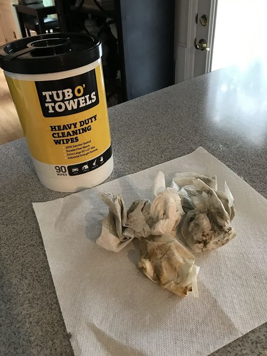 A container of wipes next to a set of wipes covered in dirt and debris after cleaning.
