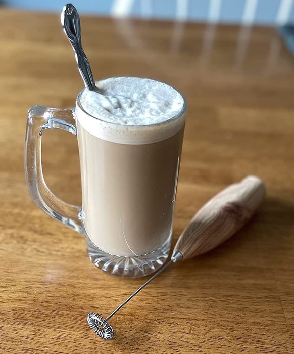 A reviewer photo featuring the frother with coffee in a clear glass topped with frothy milk.