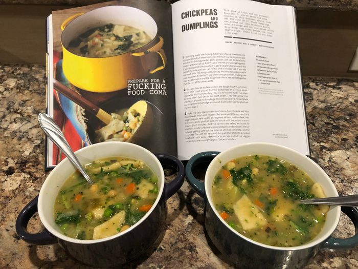 two bowls of soup resting in front of an open cookbook featuring a soup recipe