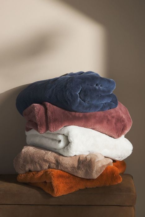 A stack of blankets in various colors: blue, mauve, white, tan, and orange