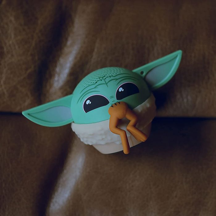 An image featuring a speaker designed to resemble Baby Yoda enjoying a frog.