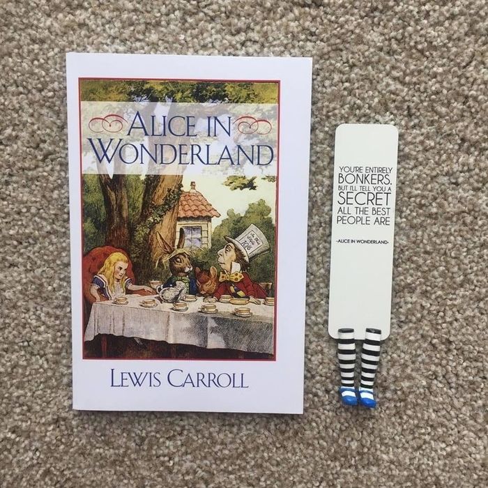A photo of a bookmark featuring a quote from Alice in Wonderland, placed beside the book by Lewis Carroll.