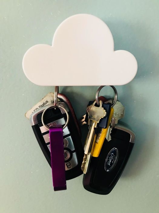 A sleek cloud-shaped magnet attached to a wall, securely holding two pairs of car keys.