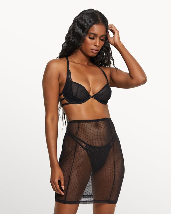 The model is showcasing a chic black thong and bra set, complemented by a flowing mesh skirt overlay.