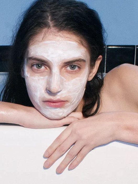 A model with fair skin and dark hair, wearing a mask on her face.