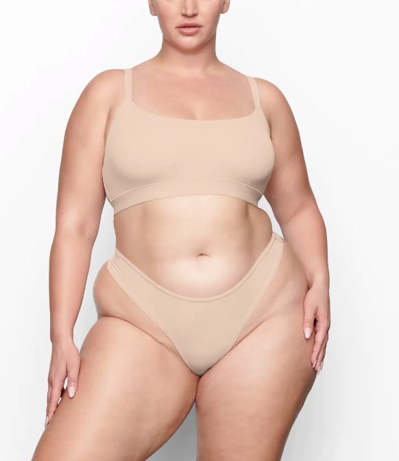 A plus-size model models a tan bralette and coordinating underwear.