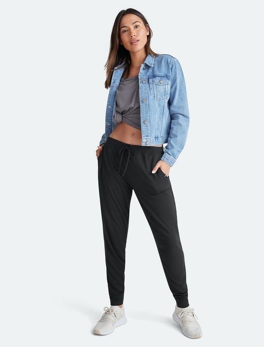 A model wearing black jogger pants paired with a denim jacket and sneakers.