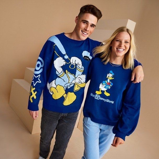 A model wearing the sweater next to another model in a blue Donald Duck sweatshirt