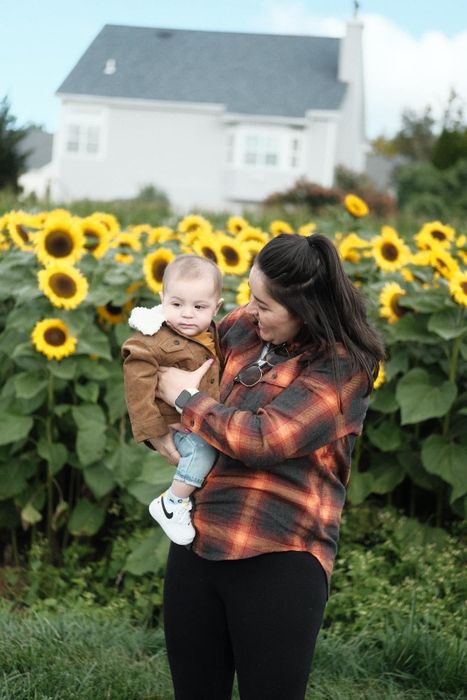 Mytour editor dressed in an orange and black flannel, holding a baby in front of a field of sunflowers
