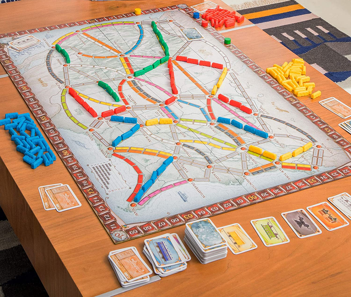 a setup table featuring the game board, playing cards, and train car pieces arranged for play 