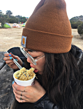 Another reviewer enjoying a bowl of ramen while wearing the brown beanie.