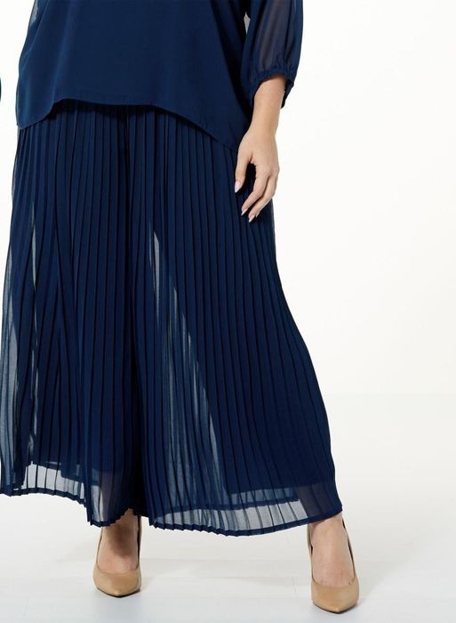 A model showcasing navy pleated pants with a skirt overlay, paired with a matching blouse.