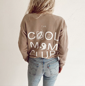 A model sporting a beige pullover sweatshirt with the inscription, 