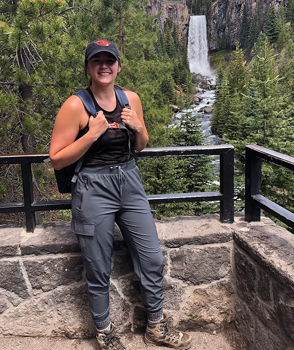 A reviewer wearing the gray joggers while hiking next to a beautiful waterfall.