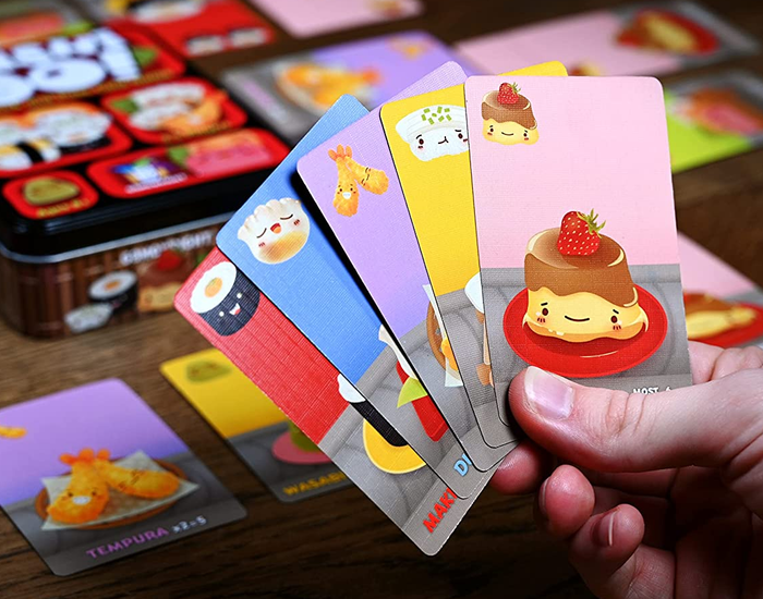 a person holding five playing cards, each adorned with a different type of sushi illustration 