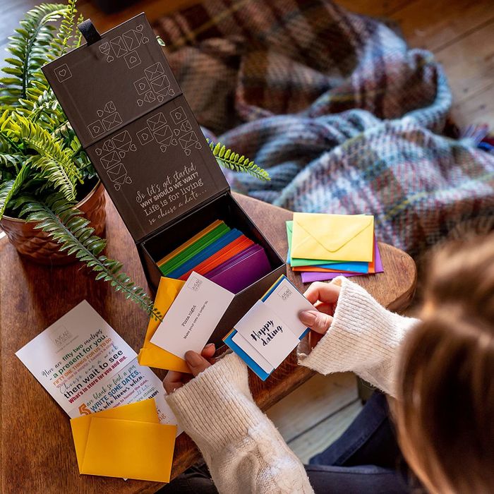 A woman unwrapping a box filled with colorful envelopes containing various date ideas.