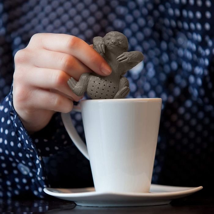 A hand carefully placing the sloth-shaped tea infuser into a white coffee mug.