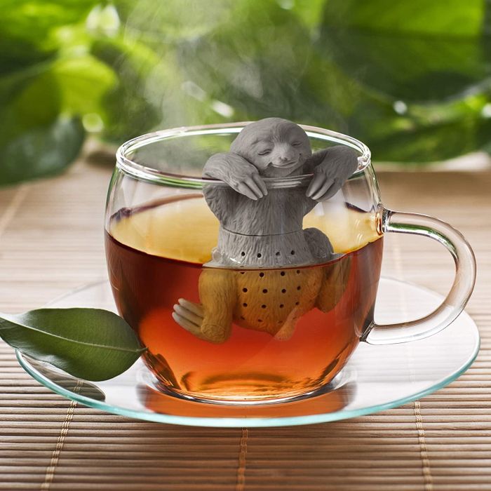 Sloth-shaped tea infuser dangling on the edge of a clear tea cup