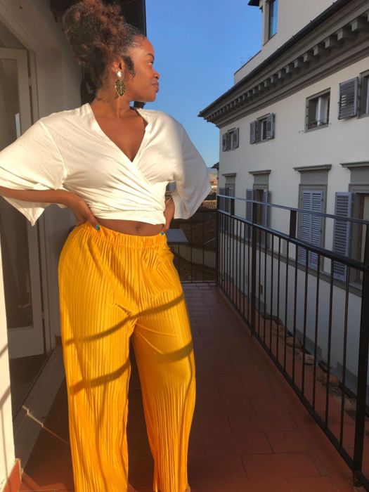 A reviewer posing on a balcony, rocking yellow pleated palazzo pants.