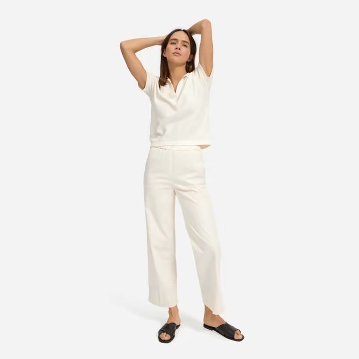 A model rocking a crisp white outfit, featuring white pants, a white top, and black shoes.