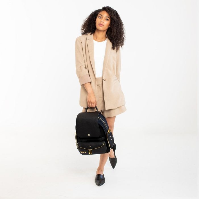 A model is seen holding a chic black backpack featuring gold zipper accents.
