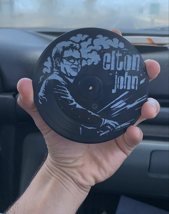 A reviewer showing off an Elton John vinyl record coaster.