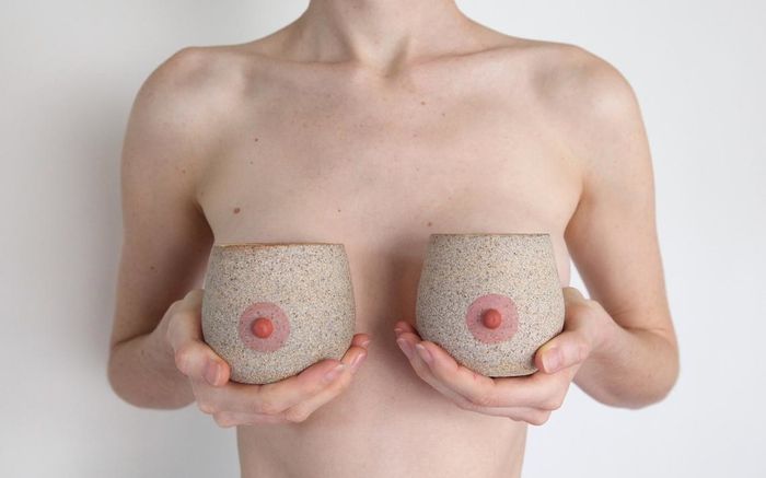 Person holding breast-shaped mugs against their chest, creating a playful and cheeky visual