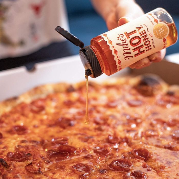 A person drizzling Mike's Hot Honey over a pizza