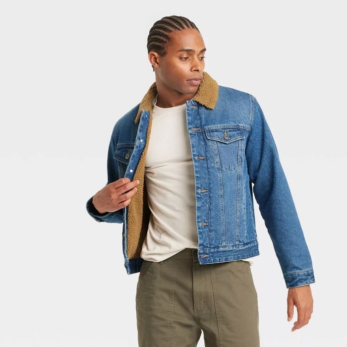 A man modeling a sherpa-lined denim jacket, paired with a beige shirt and green pants, showcasing a relaxed look ideal for a shopping feature