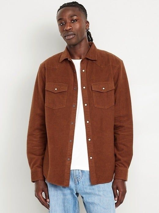 A model wearing a corduroy button-up shirt with chest pockets, layered over a basic T-shirt and paired with jeans