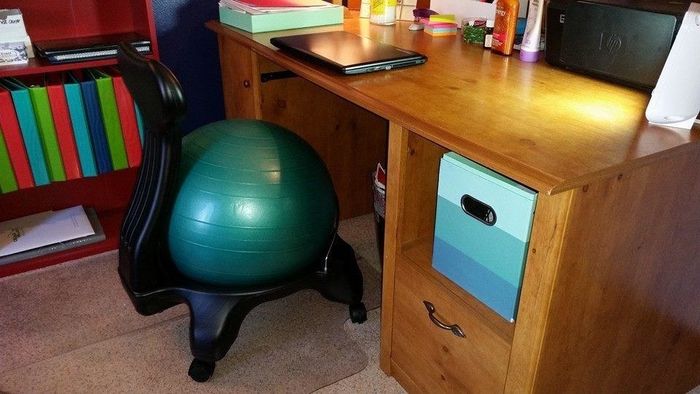 A photo showing a green balance ball with a black stand, placed in front of a desk.