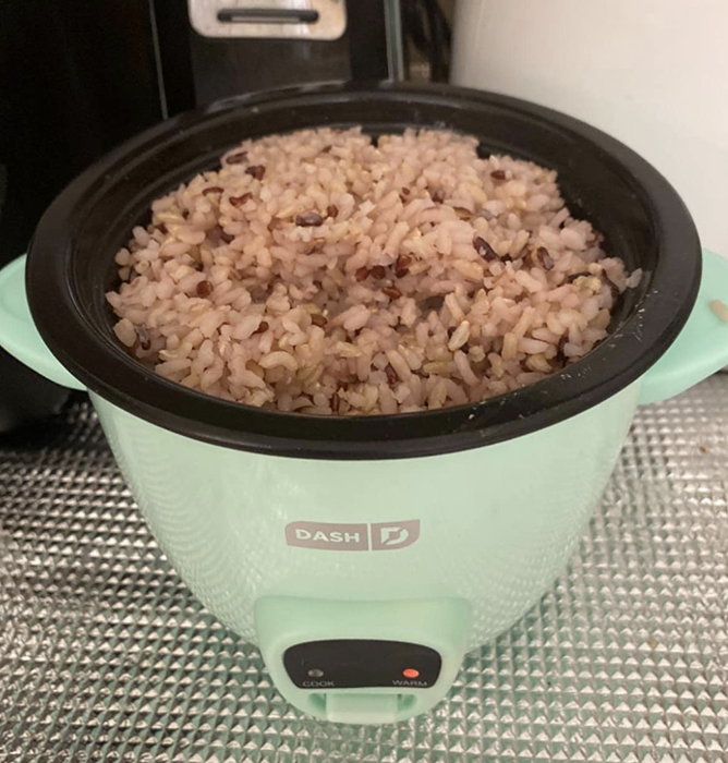 A reviewer showing the light blue rice cooker in action, cooking rice.