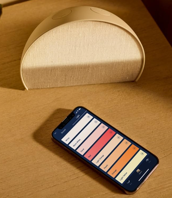 The alarm clock placed beside a phone displaying an app that allows you to control the clock's light color.