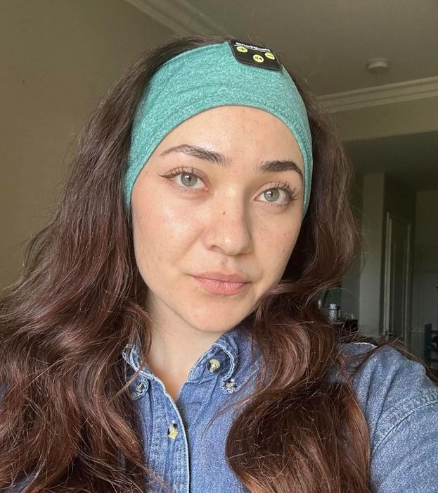 A reviewer wearing over-the-ear cloth headphones with a control panel positioned on their forehead.