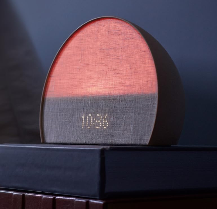 An alarm clock emitting a soft red glow with a fabric-covered digital display showing the time.