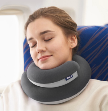 A person sleeping in an airplane seat, using a Vedta neck pillow for support.