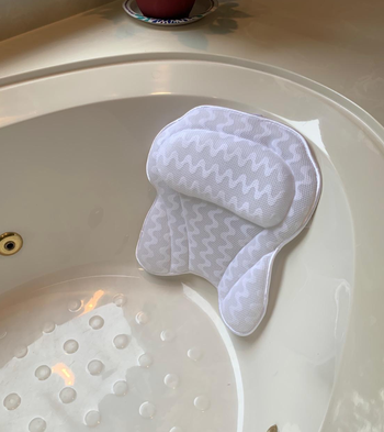 A bathtub with a white ergonomic bath pillow securely attached to the tub's edge, offering ideal head and neck support during a relaxing soak.